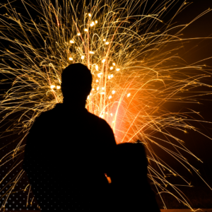 Person silhouetted against a backdrop of bright, colorful fireworks at night