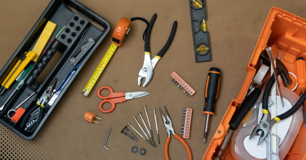 tools neatly arranged on a surface, including pliers, screwdrivers, a measuring tape, scissors, a level, and other small hardware items 